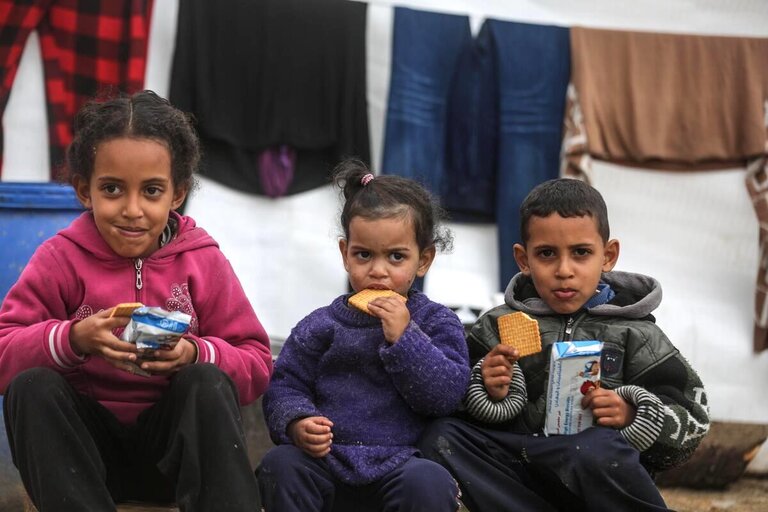 Tre bambini seduti mangiano biscotti del WFP
